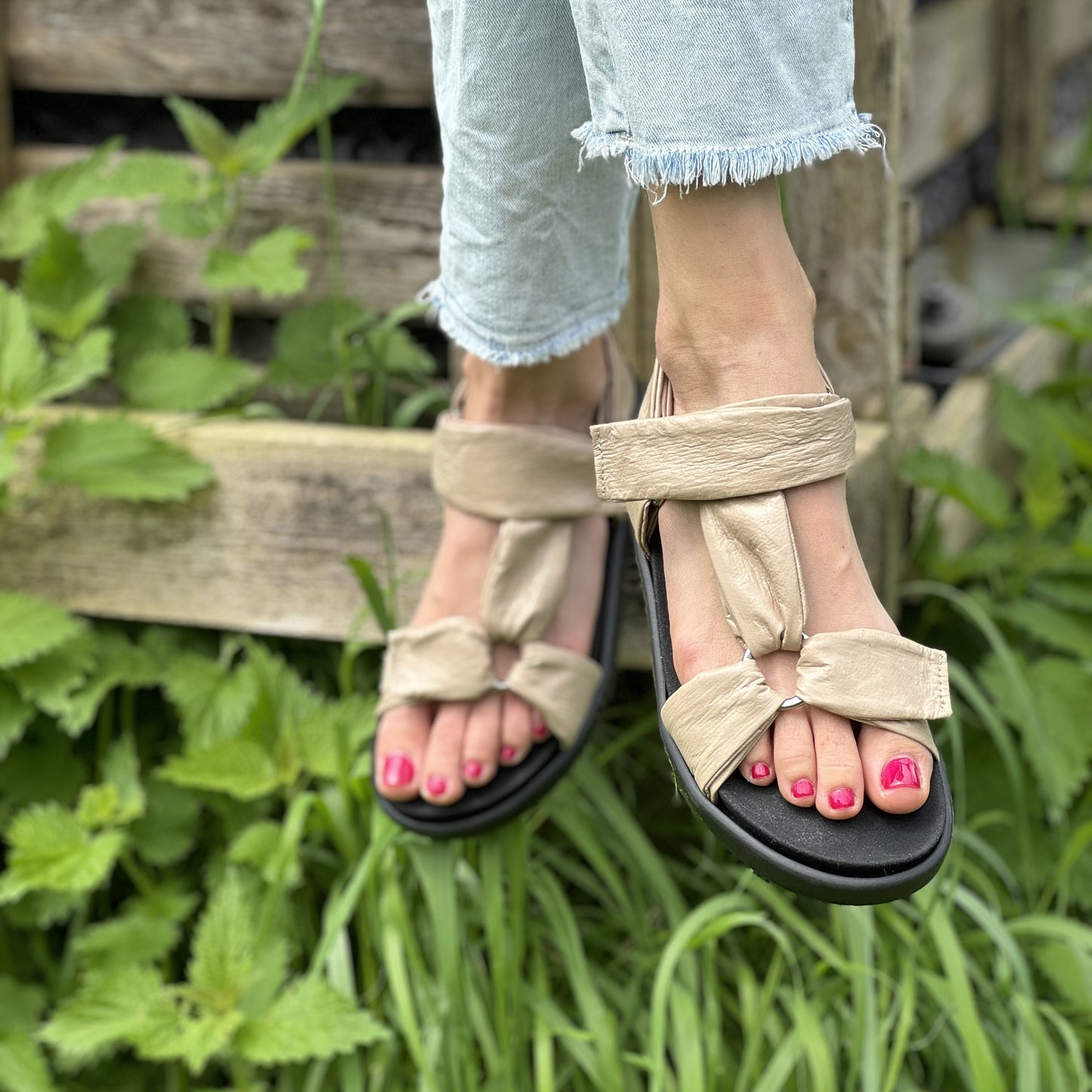 Das Model trägt eine beige Trekkingsandale, deren Fußbett sich mit einer orthpädischen Einlage wechseln lässt.